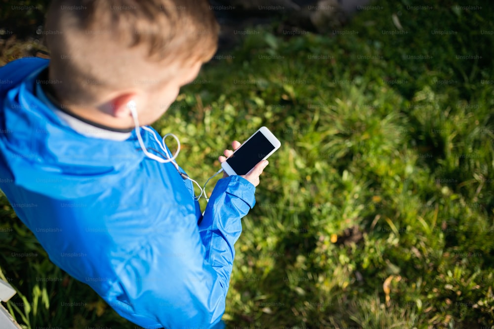 Unrecognizable runner with smart phone and earphones, listening music or using a fitness app. Using phone app for tracking weight loss progress, running goal or summary of his run. Outside in sunny autumn nature.