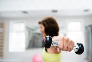 Mujer mayor con ropa deportiva en gimnasio haciendo ejercicio con pesas. Primer plano de las manos.