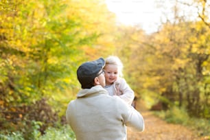 Pai segurando sua filhinha, girando-a. Caminhe na colorida floresta de outono.