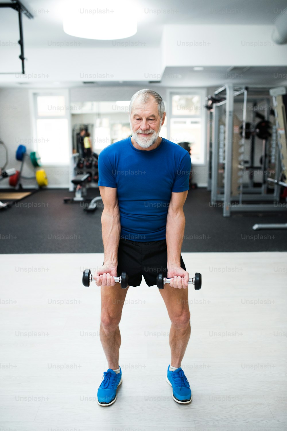 Hombre mayor con ropa deportiva en el gimnasio haciendo ejercicio con pesas