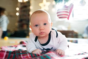 Süßer kleiner Junge unter dem Weihnachtsbaum liegt auf karierter Decke.