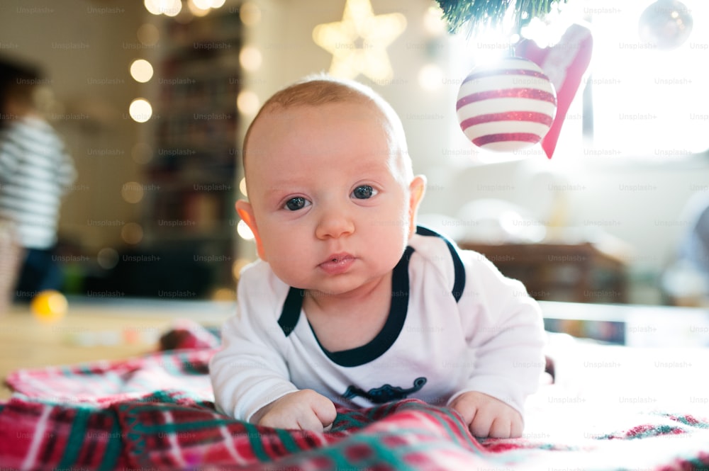 Bambino carino sotto l'albero di Natale sdraiato su una coperta a quadri.