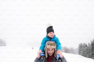 Young father outside giving his son piggyback. Having fun with his son, playing in the snow. Foggy white winter nature.