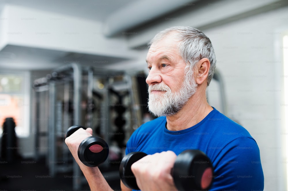 Uomo anziano in abbigliamento sportivo in palestra che si allena con i pesi.