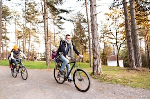 Beautiful young family with two daughters in bicycle seats in warm clothes cycling outside in autumn nature