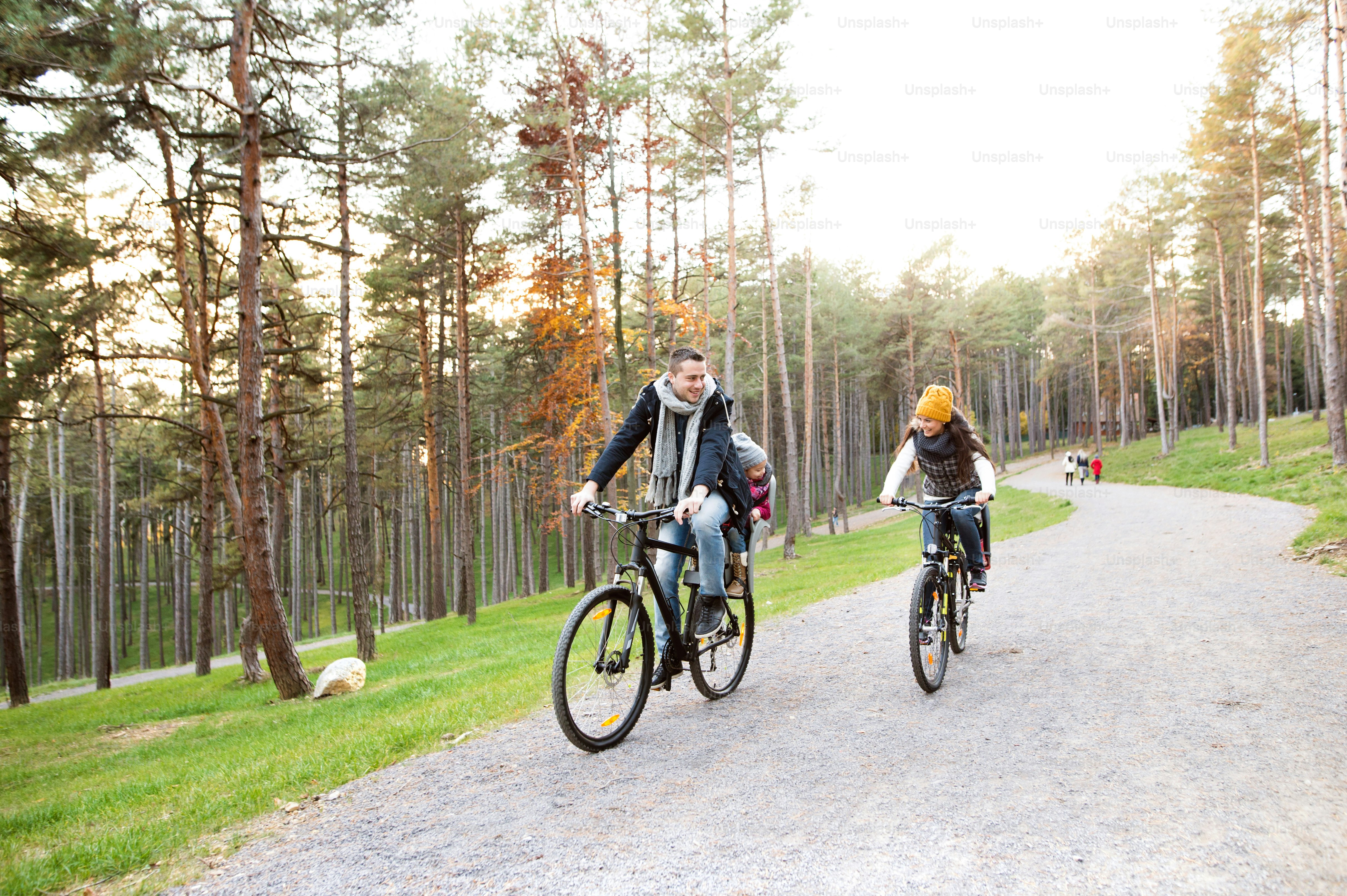 Beautiful young family with two daughters in bicycle seats in warm clothes cycling outside in autumn nature