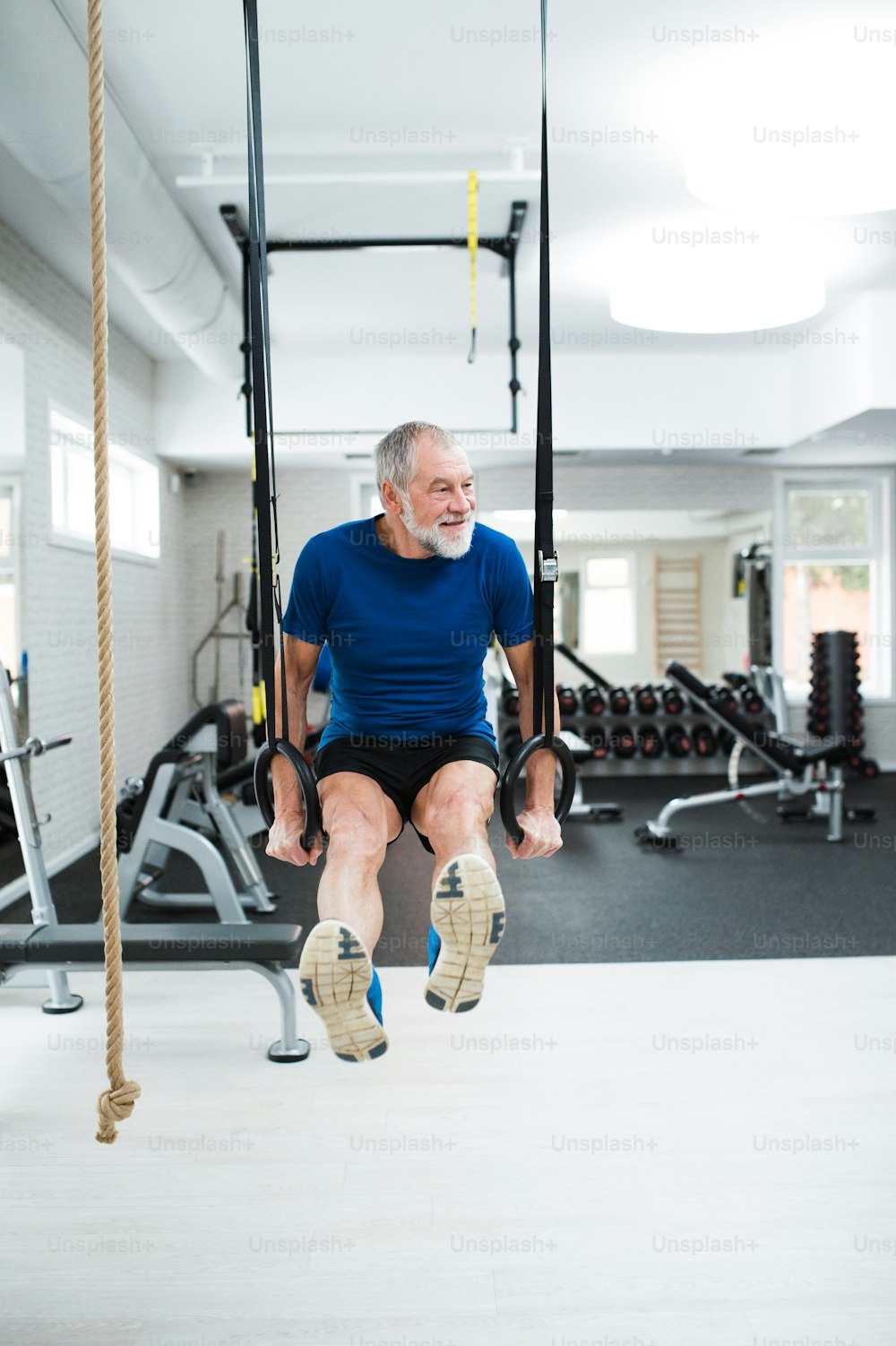 Hombre mayor con ropa deportiva en el gimnasio haciendo ejercicio en las anillas de gimnasia.