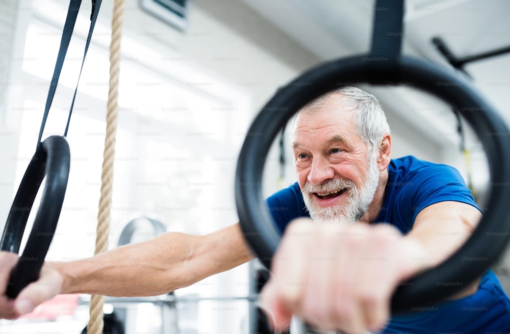 体育館で体操のリングで運動するスポーツ服を着た年配の男性。手の接写。