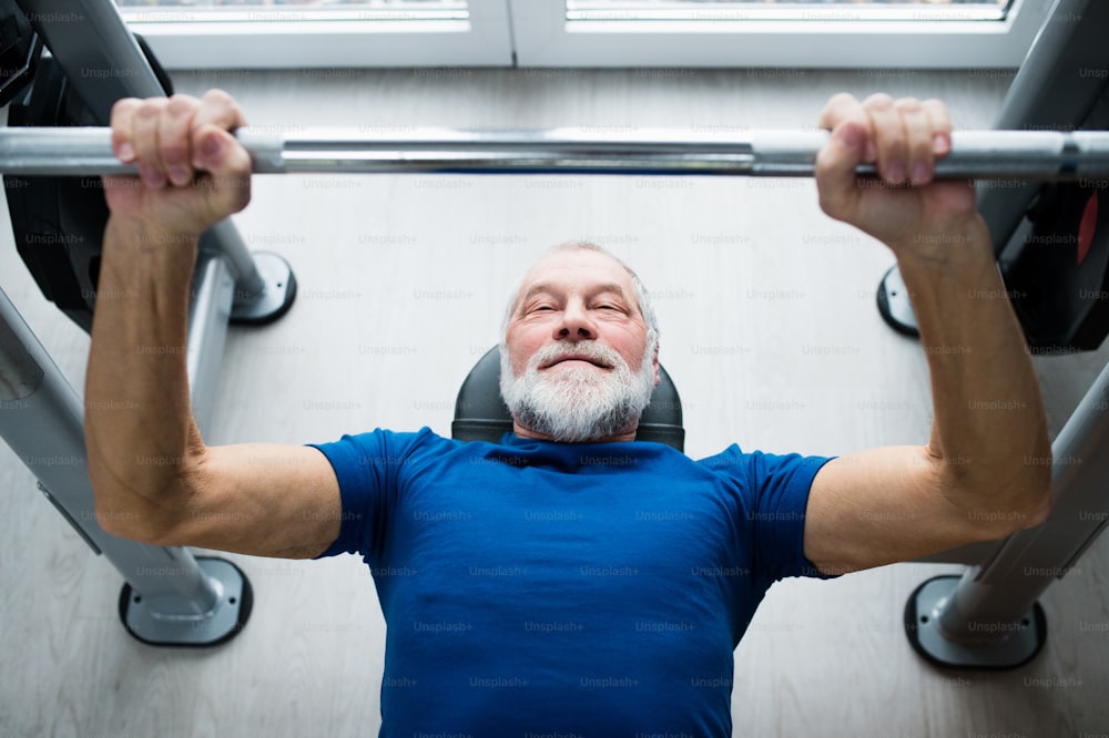 Hombre mayor con ropa deportiva en el gimnasio haciendo ejercicio con pesas, press de banca.
