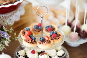 Brown wooden table with fresh fruit tarts with chocolate cream and cupcakes on cakestand. Studio shot.
