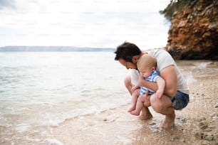 Beau jeune homme tenant son bébé à la plage profitant du temps au bord de la mer.