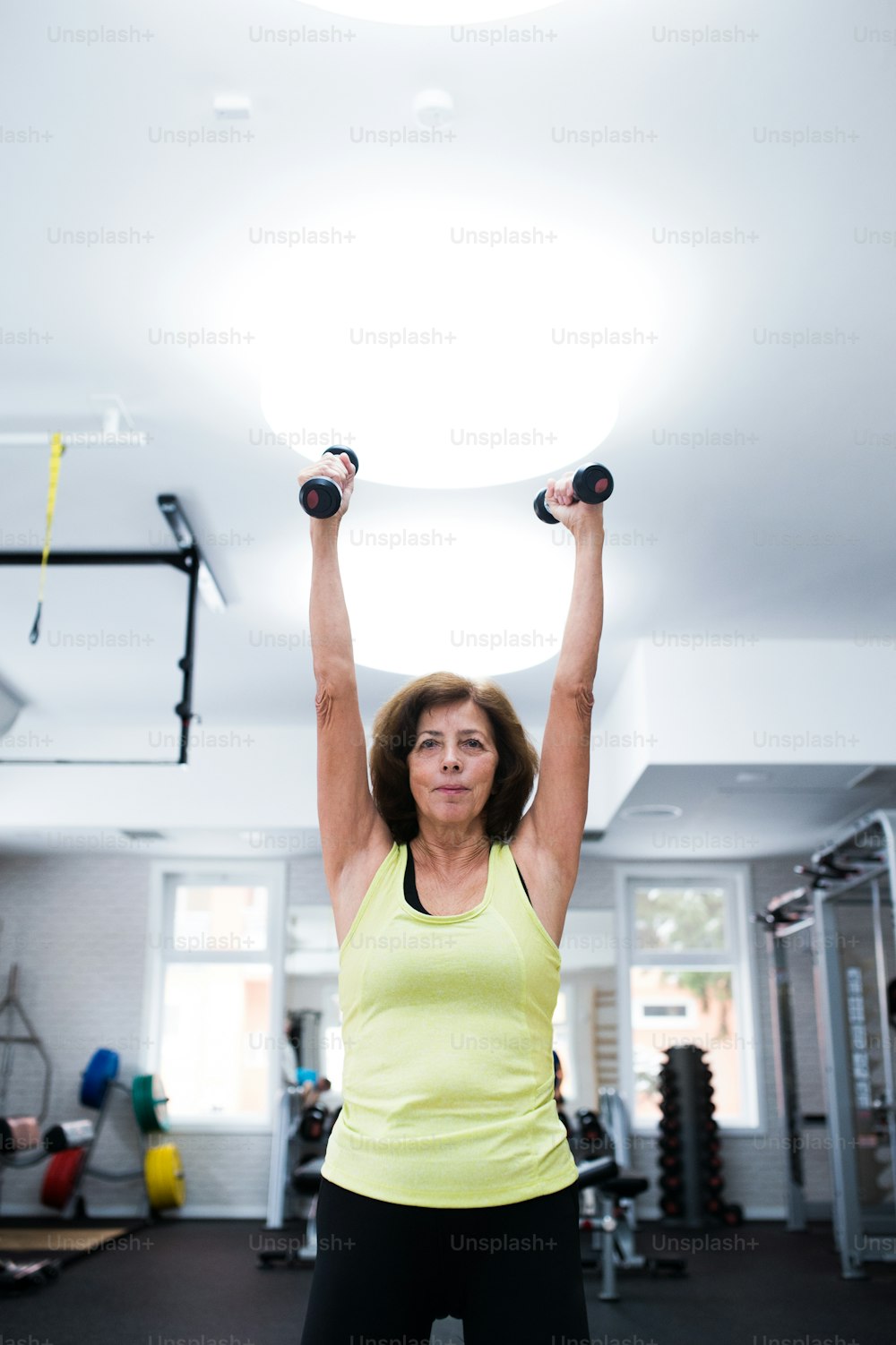 Senior woman in sports clothing in gym working out with weights. Close up of hands.