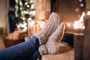 Füße einer nicht wiederzuerkennenden Frau in Wollsocken am Weihnachtskamin. Winter- und Weihnachtsurlaubskonzept.
