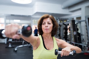 Ältere Frau in Sportkleidung im Fitnessstudio trainiert mit Gewichten. Nahaufnahme der Hände.
