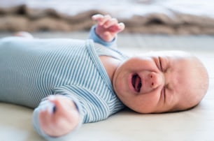 Lindo bebé recién nacido en mameluco de rayas azules acostado en la cama, llorando. Cerrar.