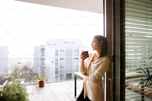 Hermosa mujer joven que se relaja en el balcón con vista a la ciudad sosteniendo una taza de café o té