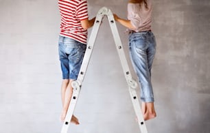 Nicht wiederzuerkennendes junges Paar steht auf einer Leiter und streicht Wände in ihrem neuen Haus. Home Makeover und Renovierungskonzept. Rückansicht.