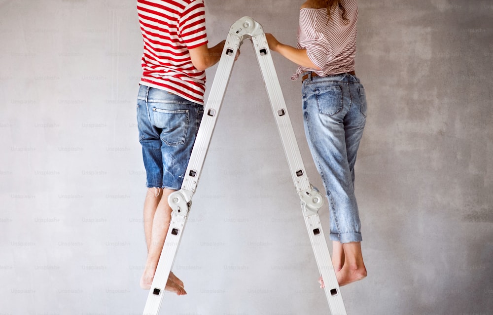 Una pareja joven irreconocible parada en una escalera pintando paredes en su nueva casa. Concepto de renovación y renovación del hogar. Vista trasera.