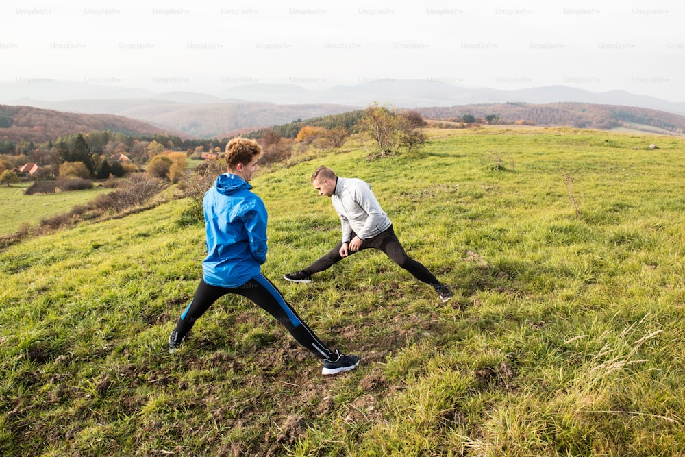 Two young handsome hipster runners in sports jackets in sunny autumn nature, resting, stretching legs