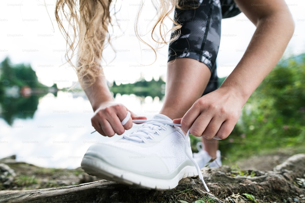 Close up of an unrecognizable young runner tying shoelaces, green nature