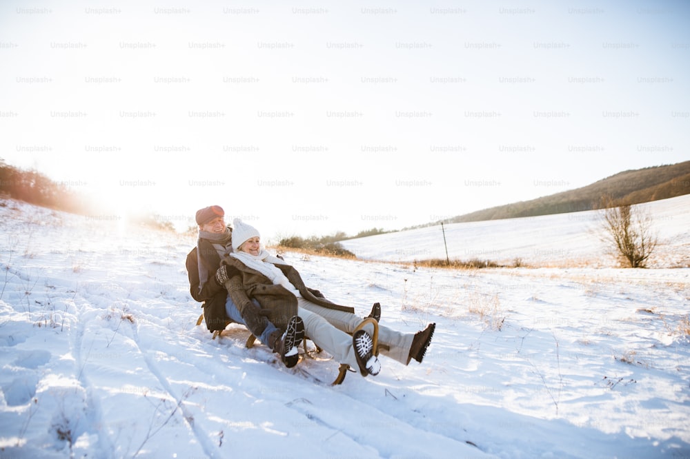 Belle femme âgée et homme sur le traîneau s’amusant dans la nature hivernale ensoleillée.