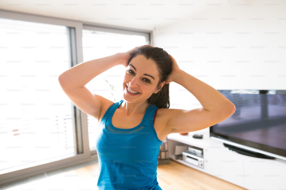 Beautiful young woman working out at home in living room, doing yoga or pilates exercise, stretching neck.