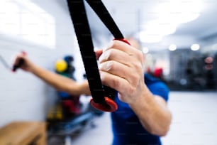 Fit senior man in sports clothing in gym working out with resistance bands. Close up of his arm.
