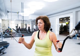 Beautiful fit senior woman in sports clothing in gym working out with resistance bands.
