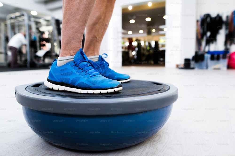 Close up of legs of senior man in gym standing on bosu balance ball and exercising as part of bodybuilding training