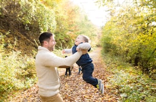 Vater hält seinen kleinen Sohn, spinnt ihn. Wandern Sie im bunten Herbstwald.