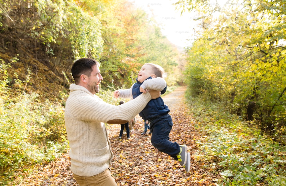 Pai segurando seu filhinho, girando-o. Caminhe na colorida floresta de outono.