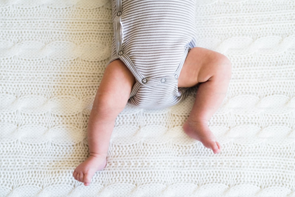 Bebé irreconocible acostado en la cama, primer plano de sus piernas