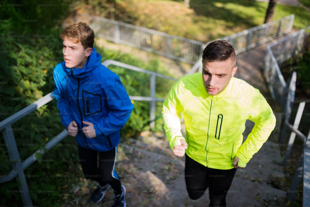 Two young athletes running on stairs outside in colorful sunny autumn nature.Trail runners training for cross country race.