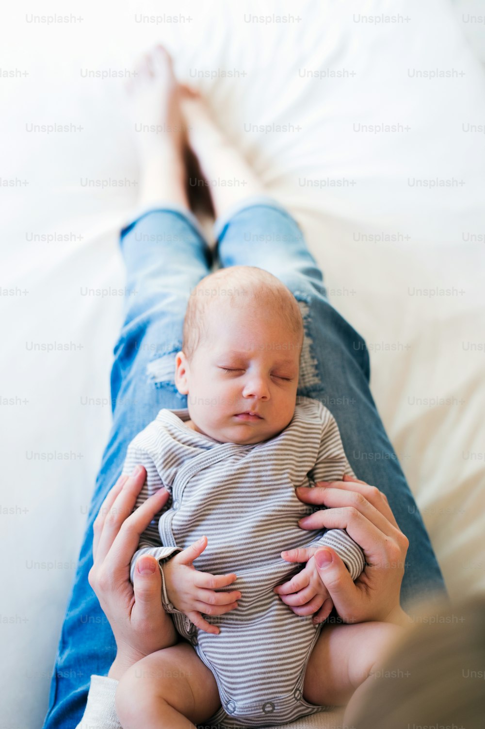 Giovane madre irriconoscibile sdraiata a letto in camera da letto, tenendo in grembo il figlio neonato addormentato