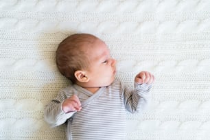 Cute newborn baby boy in striped onesie lying on bed, close up