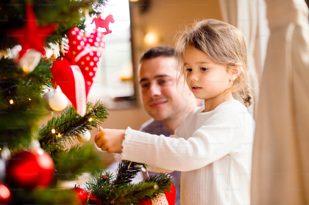 Junger Vater mit seiner kleinen Tochter zu Hause schmücken Weihnachtsbaum zusammen.