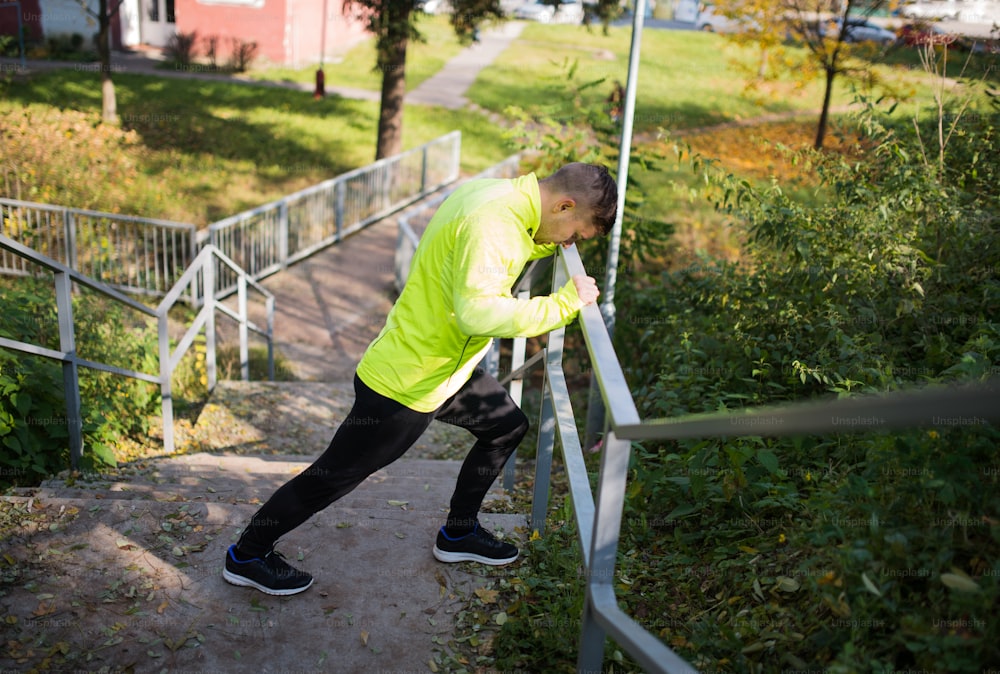 Young athlete on stairs outside in colorful sunny autumn nature, stretching legs, warming.Trail runner training for cross country race.