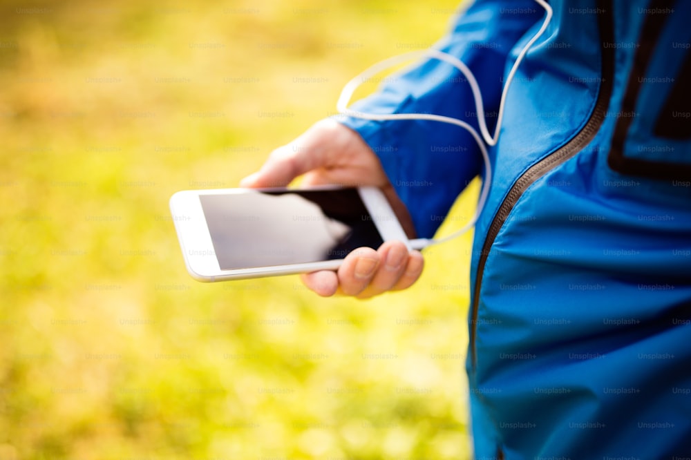 Unrecognizable runner outside in sunny autumn nature using a fitness app on his smartphone. Using phone app for tracking weight loss progress, running goal or summary of his run.