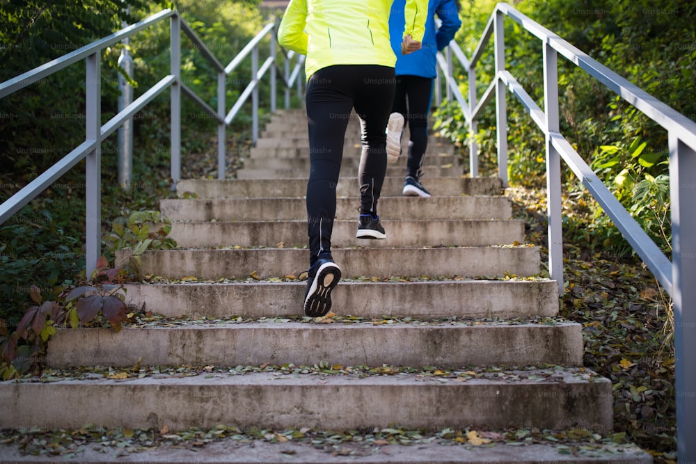 Jambes de deux jeunes athlètes méconnaissables courant dans les escaliers à l’extérieur par une journée ensoleillée colorée. Coureurs de trail s’entraînant pour la course de cross-country.