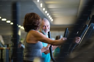 Beautiful fit senior couple in sports clothing in gym doing cardio workout, exercising on elliptical trainer machine. Sport fitness and healthy lifestyle concept.