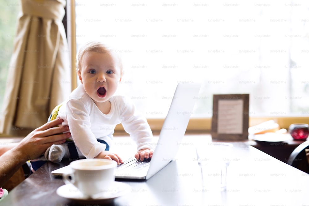 Jeune homme méconnaissable avec un cahier dans un café assis à la table en train de prendre un café, tenant son mignon bébé fils