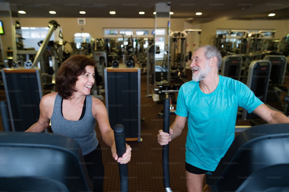 Beautiful fit senior couple in sports clothing in gym doing cardio workout, exercising on elliptical trainer machine. Sport fitness and healthy lifestyle concept.