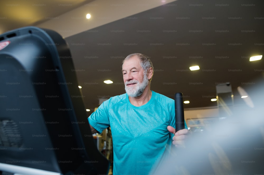 Uomo anziano in forma in abbigliamento sportivo in palestra che fa allenamento cardio, esercitandosi su una macchina ellittica per trainer. Concetto di fitness sportivo e stile di vita sano.