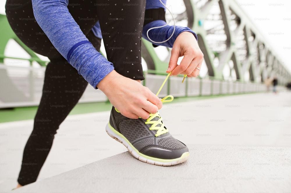 Unrecognizable runner in the city tying shoelaces on green steel bridge. Close up.