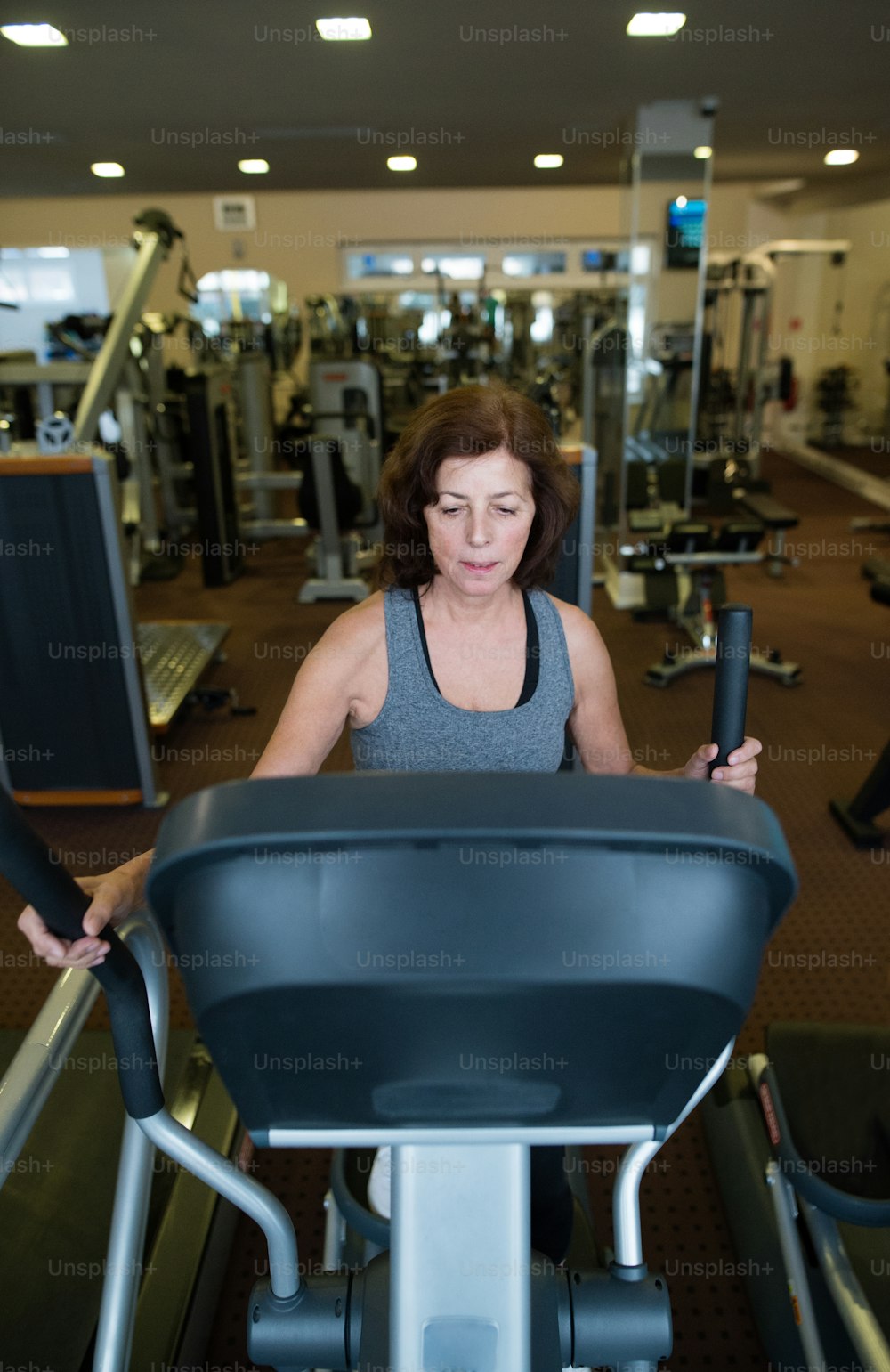 Beautiful fit senior woman in sports clothing in gym doing cardio workout, exercising on elliptical trainer machine. Sport fitness and healthy lifestyle concept.