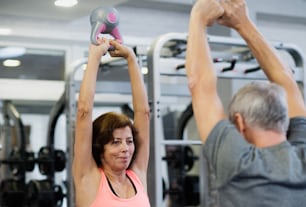 Beau couple de personnes âgées en forme dans la salle de sport s’entraînant à l’aide de kettlebells.