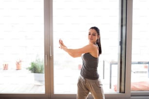 Bella giovane donna che si allena a casa in salotto, facendo esercizi di yoga o pilates, allungando le braccia.
