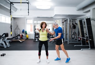 Beautiful fit senior couple in sports clothing in gym working out with weights, husband instructing his wife