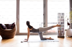 Beautiful young woman working out at home in living room, doing yoga or pilates exercise.