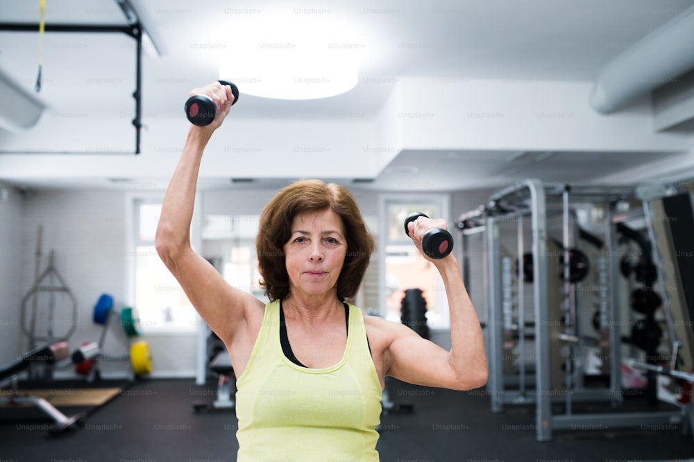 Mujer mayor con ropa deportiva en gimnasio haciendo ejercicio con pesas.